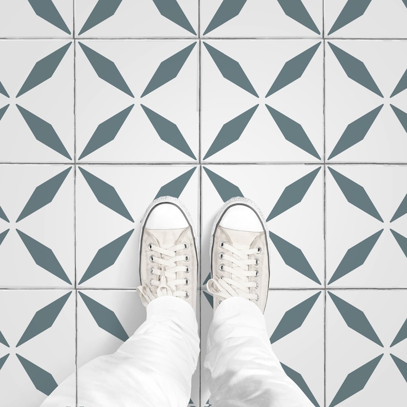 May include: Overhead shot of a person's feet wearing light-colored canvas sneakers on a tiled floor. The tiles are white with a repeating pattern of teal-colored diamond shapes. The person is wearing white pants.
