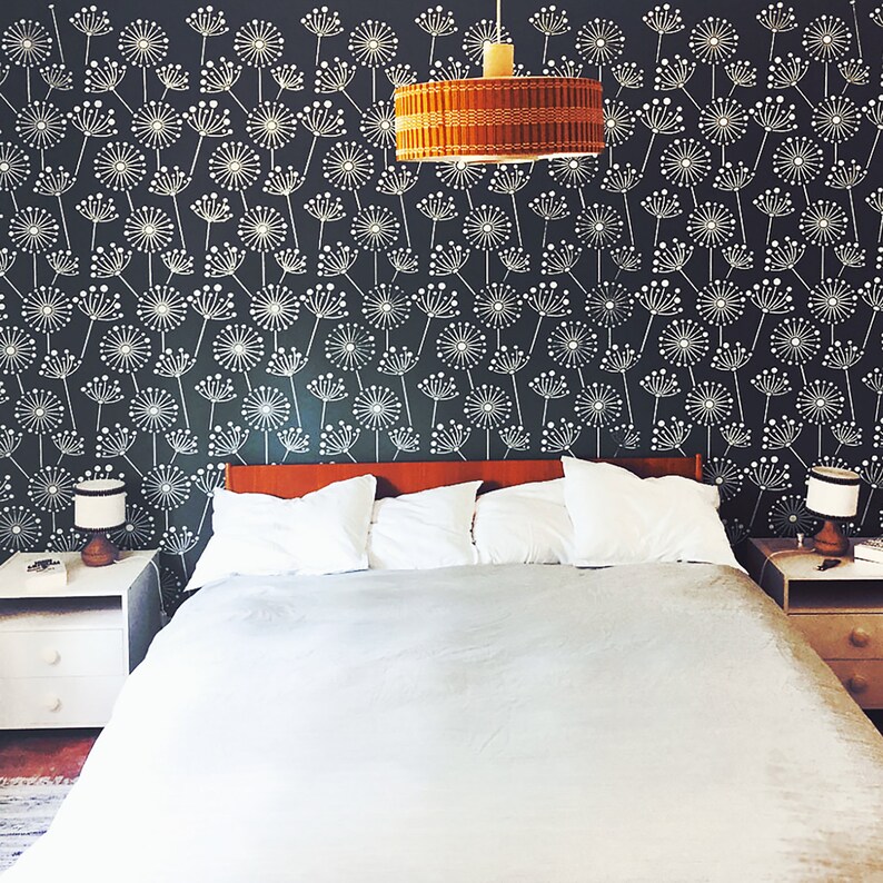K&ouml;nnte beinhalten: Schlafzimmer mit Bett, Nachttischen und gemusterter Tapete. Das Bett hat wei&szlig;e Kissen und eine graue Bettdecke. Die Wand ist dunkel mit einem wei&szlig;en Blumenmuster. &Uuml;ber dem Bett h&auml;ngt eine gewebte Pendelleuchte.