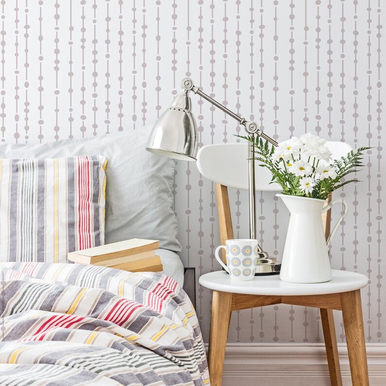 May include: A bedroom with a bed with a striped comforter and pillows. A bedside table with a lamp, a mug, and a vase of white flowers. The wall behind the bed has a light gray and white geometric pattern.