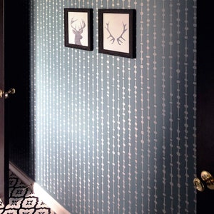 May include: A light blue wall with a white stencil pattern of vertical lines of circles. Two black framed pictures with silhouette images of deer heads are hanging on the wall.