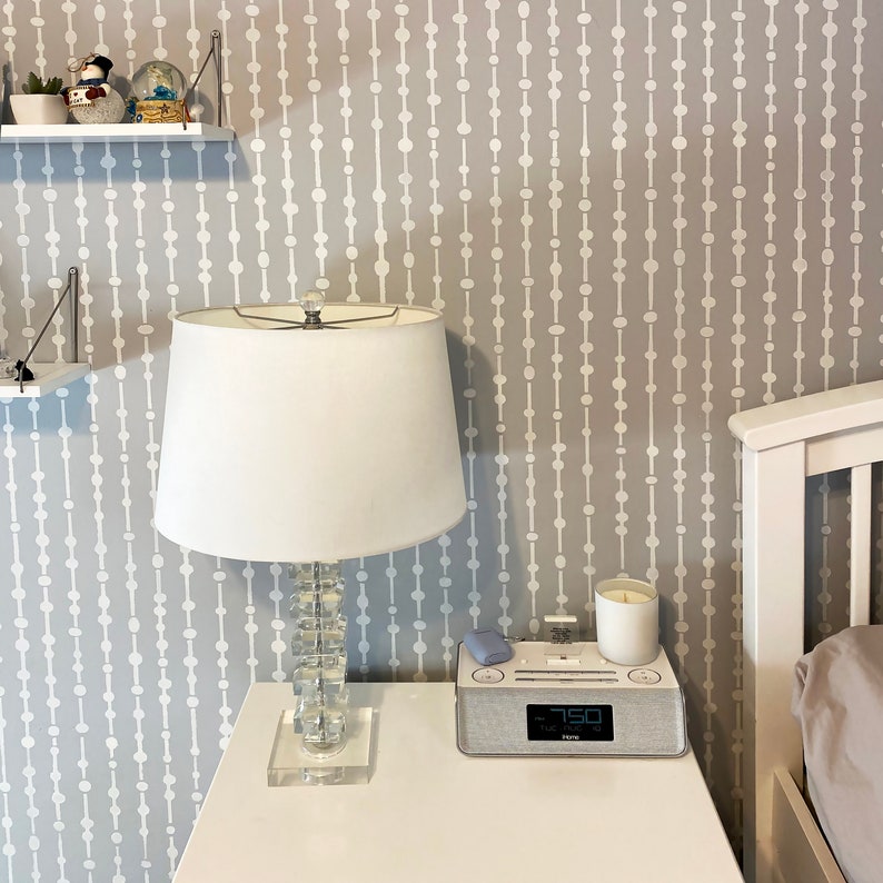 May include: A white bedside table with a white lamp with a crystal base, a white candle, a blue device, and a white clock radio with the time 7:50 displayed on it.