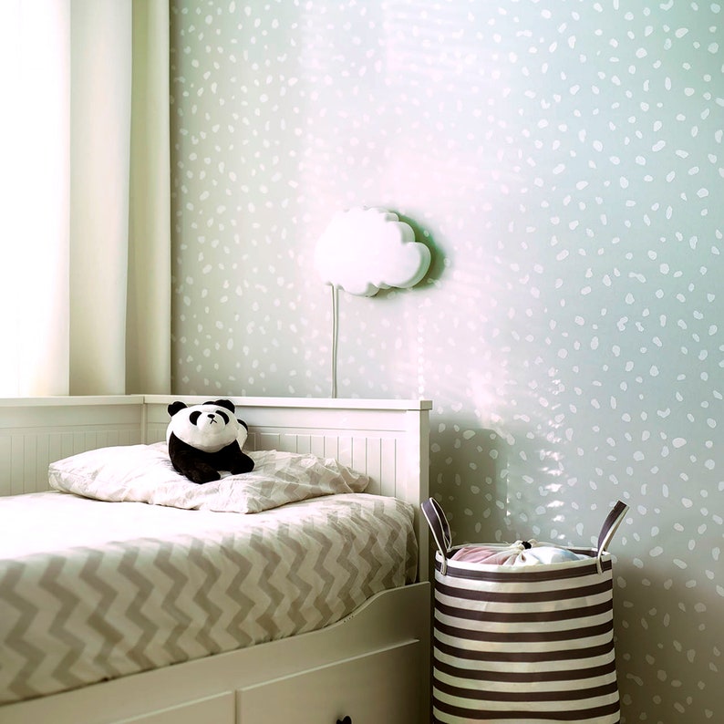 May include: A white bed with a gray and white chevron patterned bedding. A black and white panda plush toy is sitting on the bed. A white cloud-shaped nightlight is on the wall. A striped laundry basket is next to the bed.