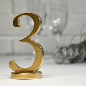 May include: Gold number three table number for a wedding or party. The number is on a gold base.