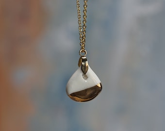 May include: A gold chain necklace featuring a teardrop-shaped pendant. The pendant has a smooth white upper section and a metallic gold-toned lower section, suspended from a small gold bail attached to the delicate link chain.