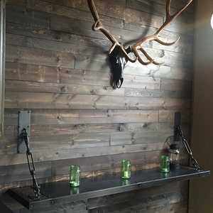 May include: A rustic wooden wall with a mounted elk antler skull and a black metal shelf with chains hanging from the wall. The shelf has three glass jars on it.