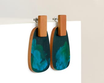 May include: A pair of dangle earrings with a dark green and teal resin oval shape and a wooden top piece.