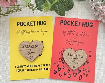 Könnte beinhalten: Zwei Pocket Hug Karten, eine gelbe und eine rote, mit Holzherzakzenten. Auf der gelben Karte steht "Amazing Son" und auf der roten Karte steht "A Little Hug From Mum". Beide Karten haben oben die Worte "Pocket Hug".