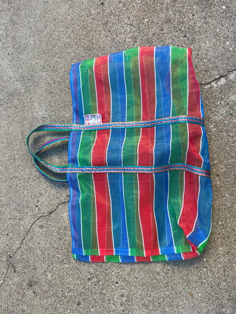 May include: A colorful tote bag with vertical stripes in red, green, and blue. The bag has a rectangular shape with a handle and a decorative trim. The bag is made of a mesh-like material.