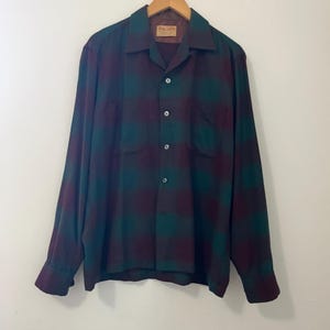 May include: A long-sleeved button-down shirt with a plaid pattern in shades of green and burgundy.