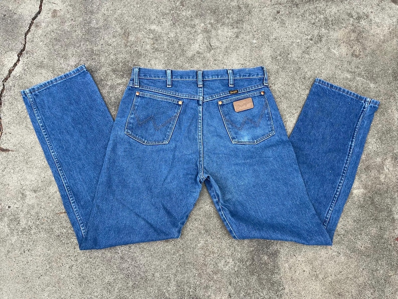 Puede incluir: Un par de pantalones vaqueros azules de mezclilla con un parche de cuero marr&oacute;n en el bolsillo trasero que dice "Wrangler".