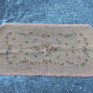 Puede incluir: Una alfombra rectangular rosa con un diseño floral bordado en tonos de rosa, azul y verde. La alfombra tiene un borde deshilachado.