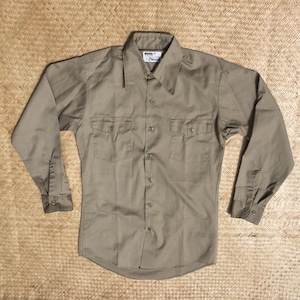 May include: A long-sleeved, olive green work shirt with two chest pockets and a button-down collar.