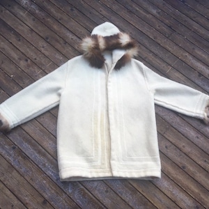 May include: A white hooded parka with a brown fur trim around the hood and cuffs. The parka has a zipper closure and a long, straight cut.