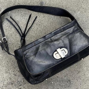 May include: A black leather shoulder bag with a silver clasp. The bag has a flap closure and a long strap.