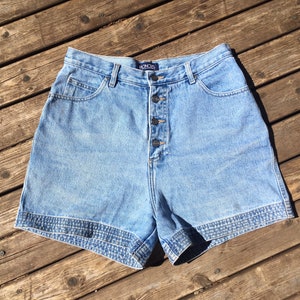 May include: Light blue denim shorts with a button fly and a single back pocket. The shorts have a decorative trim around the hem.