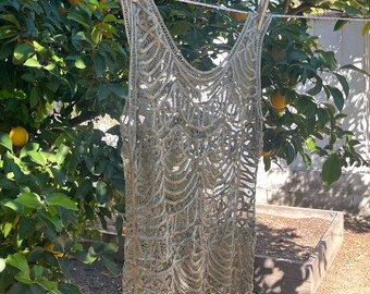 Könnte beinhalten: Ein hellgrünes, offen gewebtes Kleid hängt an einer Wäscheleine mit Holzklammern. Das Kleid hat ein detailliertes, spitzenartiges Muster. Der Hintergrund zeigt einen üppigen grünen Baum mit gelben Früchten.