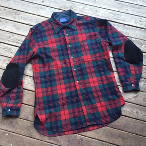 May include: A red, green, and black plaid flannel shirt with elbow patches. The shirt has a button-down collar and long sleeves.