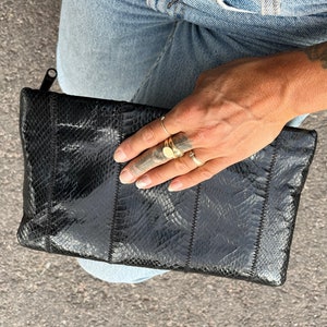 Pode incluir: Uma carteira de mão preta de pele de cobra com fecho de correr.