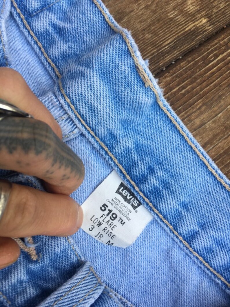 Puede incluir: Un primer plano de una etiqueta de mezclilla azul Levi's 519 flare de tiro bajo. La etiqueta es blanca con texto negro y dice "100% Algod&oacute;n Hecho en EE. UU. Cuidado en el reverso 519 TM Flare Tiro bajo 3 JR. M".