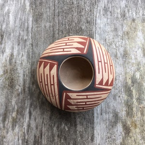 May include: A traditional Native American pottery bowl with a black and red geometric design. The bowl is round and has a wide opening.