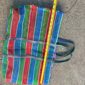May include: A colorful striped tote bag with red, green, blue, and white vertical stripes. The bag has two handles and is approximately 26 inches long. The bag is made of a mesh-like material.