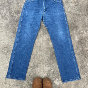 Puede incluir: Un par de pantalones vaqueros azules de mezclilla con corte recto. Los vaqueros tienen un dise&ntilde;o cl&aacute;sico de cinco bolsillos y cierre de bot&oacute;n.