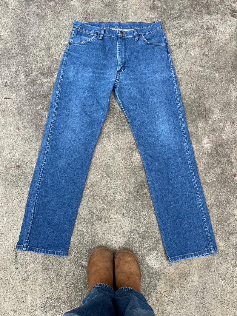 Puede incluir: Un par de pantalones vaqueros azules de mezclilla con corte recto. Los vaqueros tienen un dise&ntilde;o cl&aacute;sico de cinco bolsillos y cierre de bot&oacute;n.