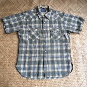 May include: A short-sleeved plaid shirt with a button-down collar and two chest pockets. The shirt is in a brown, blue, and white plaid pattern.