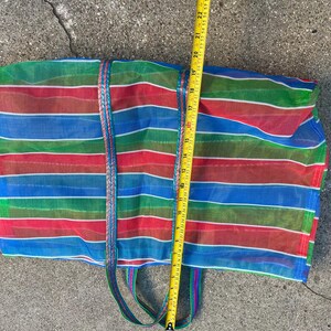 May include: A colorful, striped tote bag with red, blue, and green horizontal stripes. The bag has a braided handle and measures approximately 24 inches in length. The bag is made of a mesh material.