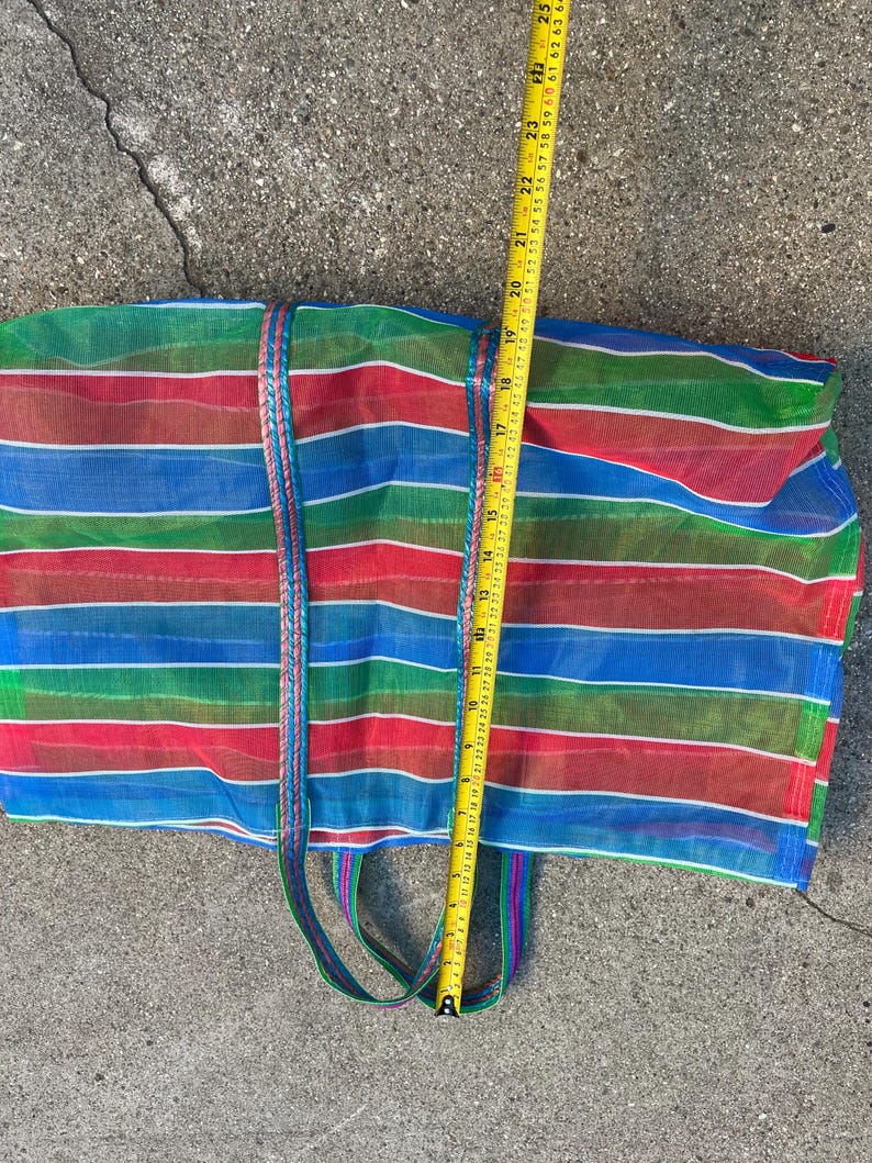 May include: A colorful, striped tote bag with red, blue, and green horizontal stripes. The bag has a braided handle and measures approximately 24 inches in length. The bag is made of a mesh material.
