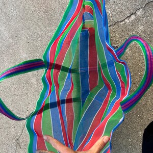 May include: A colorful striped tote bag with red, green, blue, and white vertical stripes. The bag has matching striped handles in shades of pink, green, and blue. The bag is open, revealing the interior.