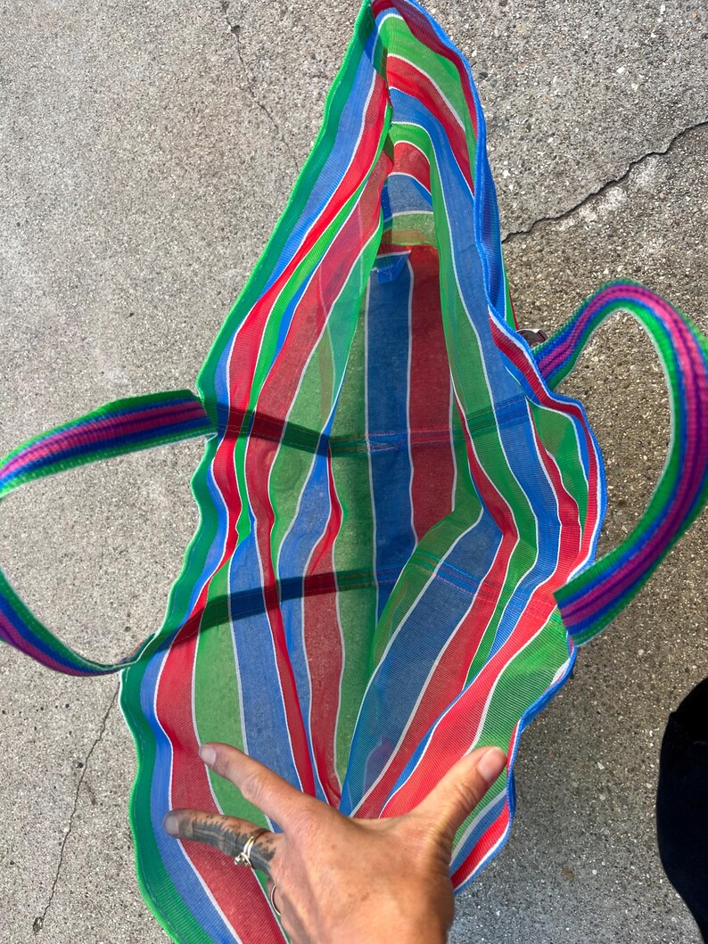 May include: A colorful striped tote bag with red, green, blue, and white vertical stripes. The bag has matching striped handles in shades of pink, green, and blue. The bag is open, revealing the interior.