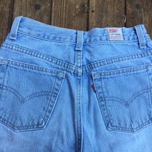Puede incluir: Un par de pantalones vaqueros de mezclilla azul claro con bolsillos traseros y una etiqueta Levi's en la parte posterior de la cintura.