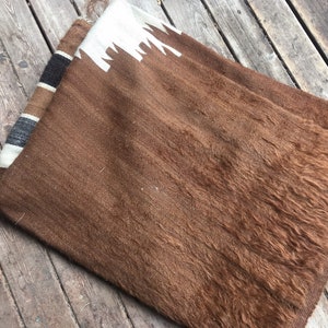 May include: A brown alpaca wool throw blanket with a white and black geometric pattern on one end.
