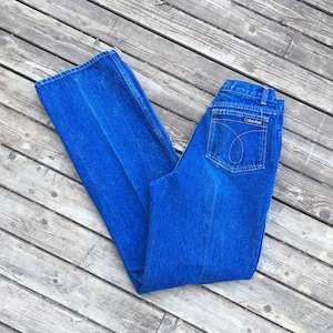 Puede incluir: Un par de pantalones vaqueros azules de mezclilla con cintura alta y pierna ancha. Los pantalones vaqueros tienen un logotipo de Calvin Klein en el bolsillo trasero.