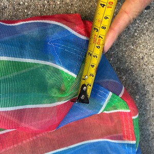 May include: Close-up of a colorful, striped mesh fabric in red, blue, green, and white. A yellow tape measure shows a measurement of approximately 4 inches. The fabric appears to be part of a larger item.