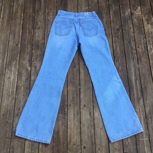 Puede incluir: Un par de pantalones vaqueros de campana de mezclilla azul claro. Los pantalones tienen cintura alta y pierna ancha.