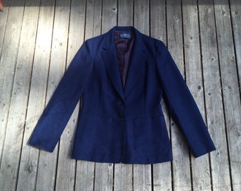 May include: A navy blue blazer with a two-button closure and two front pockets. The blazer has a notched lapel and a dark purple lining. The garment is displayed on a weathered wooden surface.