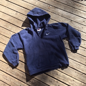May include: A navy blue hooded sweatshirt with a white Nike swoosh logo on the left chest. The sweatshirt has a kangaroo pocket and a drawstring hood.
