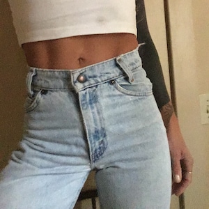 May include: A close-up of a person wearing light blue denim jeans with a high waist and a white crop top.