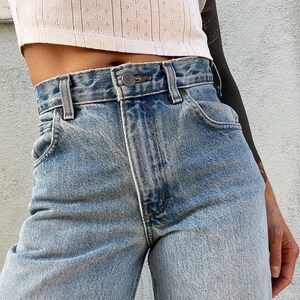 May include: Light blue denim jeans with a high waist and a button fly. The jeans are slightly faded and have a relaxed fit.