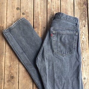 Puede incluir: Un par de pantalones vaqueros de mezclilla gris oscuro con un bolsillo trasero y una etiqueta roja.