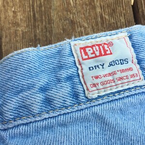 Puede incluir: Un primer plano de una cintura de mezclilla azul claro con una etiqueta Levi's blanca que dice "Dry Goods Two-Horse Brand Dry Goods Since 1853."