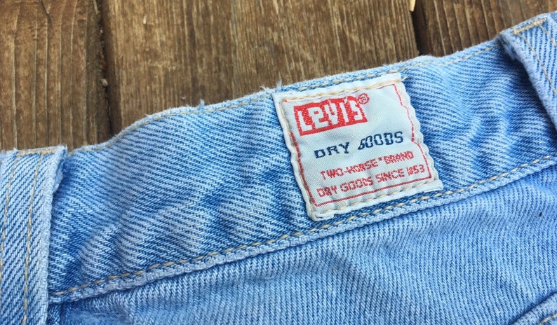 Puede incluir: Un primer plano de una cintura de mezclilla azul claro con una etiqueta Levi's blanca que dice "Dry Goods Two-Horse Brand Dry Goods Since 1853."