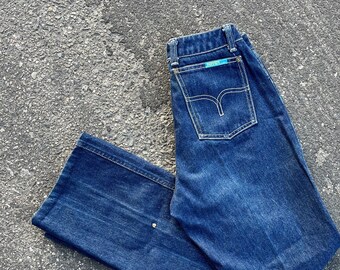 Può includere: Un paio di jeans in denim blu scuro con un'etichetta blu chiaro sulla tasca posteriore.