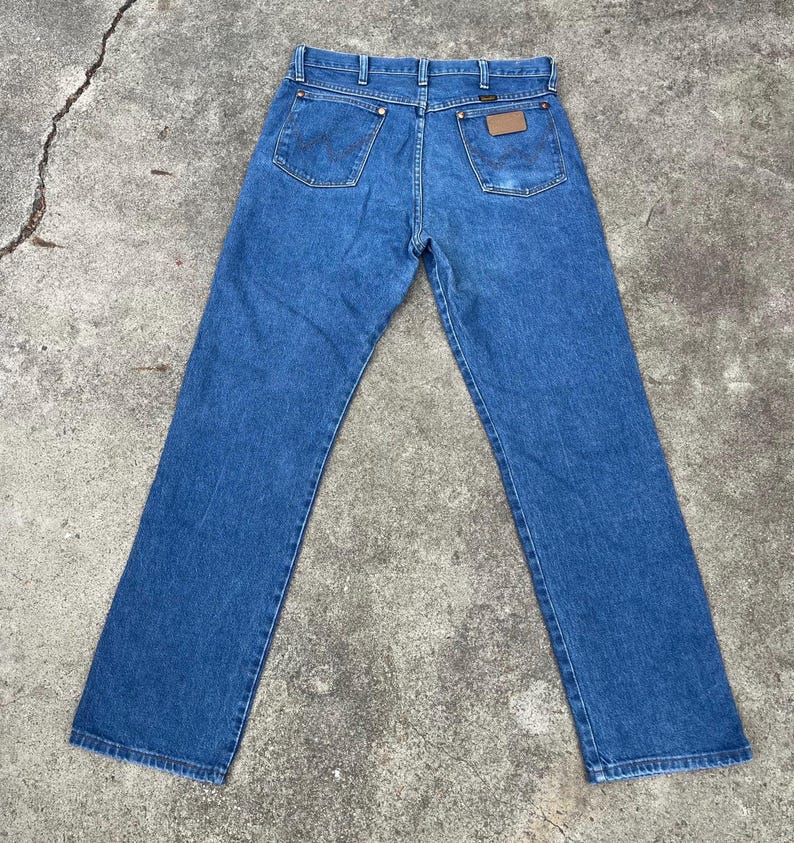Puede incluir: Un par de pantalones vaqueros azules de mezclilla con un parche de cuero marr&oacute;n en el bolsillo trasero. Los pantalones tienen una pierna recta y un ajuste cl&aacute;sico.
