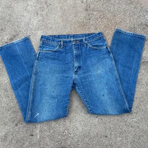 May include: Blue denim jeans with a classic five-pocket design. The jeans have a button and zip closure, belt loops, and a straight leg cut. The denim shows some wear and tear, with a few paint marks. A casual, everyday wardrobe staple.
