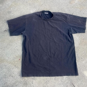 May include: A faded black t-shirt with a crew neck and short sleeves. The shirt is laid flat on a concrete surface. The fabric appears worn and soft, suggesting it has been washed multiple times.