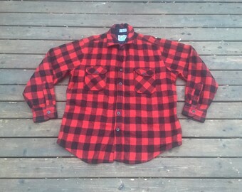 May include: A red and black plaid flannel shirt with long sleeves and two chest pockets.
