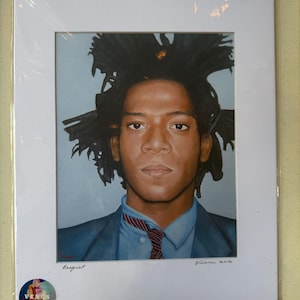 May include: A framed portrait of Jean-Michel Basquiat, depicting the artist in a blue suit and a red and blue striped tie. The artwork is signed and dated, with the word "Basquiat" written below the image. The frame is white.